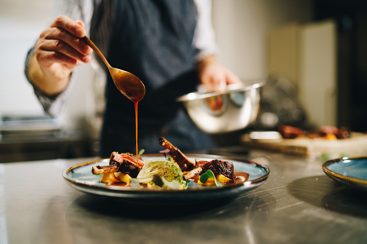 Chef pouring special sauce on pork ribs in the kitchen